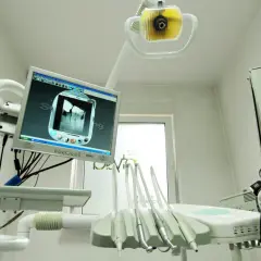 Nowoczesny gabinet stomatologiczny z aparaturą RTG i monitorem wyświetlającym zdjęcie zęba. NZOZ to skrót od Niepubliczny Zakład Opieki Zdrowotnej.