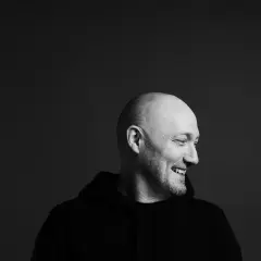 Uśmiechnięty Paul Kalkbrenner w czarnej bluzie, gotowy na koncert w Warszawie.