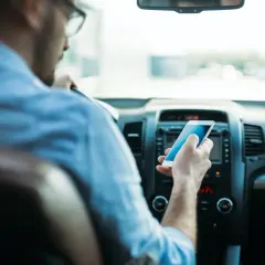 Mężczyzna w okularach trzyma telefon, sprawdzając wiadomości. Widok zza kierowcy, jakby przez lustro.
