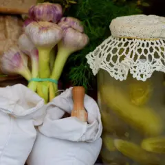 Słoik kiszonych ogórków, czosnek, koperek i białe woreczki.