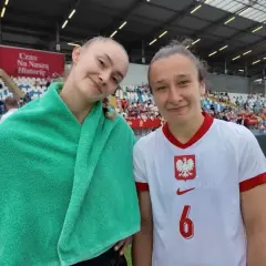 Dwie młode piłkarki w strojach reprezentacji Polski na tle trybun stadionu.