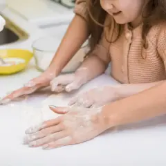 Radość z zabawy w domu z 3 latkiem. Dziecko i mama wspólnie zagniatają ciasto, ubrudzone mąką.