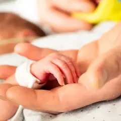 Dłoń rodzica obejmuje maleńką dłoń dziecka z zespołem Edwardsa, otoczoną troską i nadzieją.