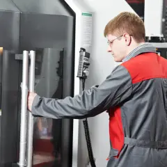 Ein Zerspanungsmechaniker öffnet die Tür einer CNC-Maschine. Er erkundet zerspanungsmechaniker weiterbildungsmöglichkeiten.