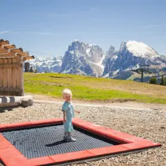 Mały chłopiec na trampolinie na tle majestatycznych gór we Włoszech.