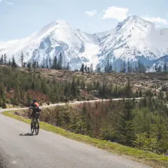 Rowerzysta na krętej drodze z widokiem na ośnieżone Tatry. Marzenie o rowerem dookoła Tatr w jeden dzień staje się rzeczywistością.