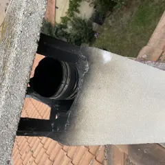 Détail d'un conduit de cheminée en métal noir, visiblement endommagé et encrassé, suggérant la nécessité de comment condamner un conduit de cheminée pour des raisons de sécurité.