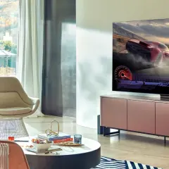 Młody mężczyzna gra w grę wyścigową na telewizorze 65 cali. Idealna odległość od telewizora 65 cali zapewnia wciągające wrażenia.