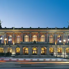 Prachtvolle alte Stadthalle im Abendlicht, beleuchtete Fenster und Türme, Lichterspuren auf der Straße.