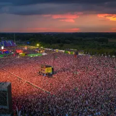 Widok z lotu ptaka na festiwal muzyczny z tłumem ludzi i sceną podczas zachodu słońca.