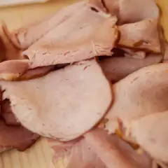 Plastry wędzonej szynki, gotowe do parzenia. Delikatne, różowe mięso z lekko zarumienionymi brzegami.