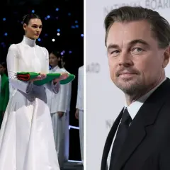 Leonardo DiCaprio na gali National Board of Review, obok modelki w białej sukni i grupy osób w zielonych strojach.