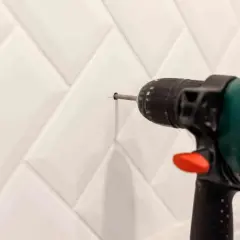 Taladro perforando un agujero en una pared con azulejos blancos para colocar tacos.