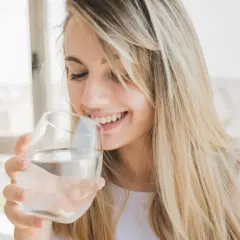 Une jeune femme souriante boit de l'eau osmosée dans un verre.