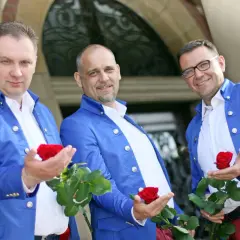 Trzech panów w niebieskich marynarkach, czyli skład zespołu Blue Party, prezentuje czerwone róże.