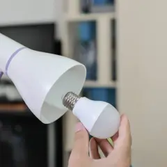 Ręka wymienia żarówkę w lampce biurkowej, symbolizując modernizację oświetlenia i oszczędność energii.