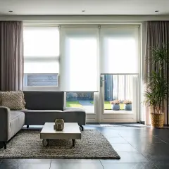 Nowoczesne zasłony do salonu inspiracje: szare, welurowe zasłony tworzą przytulną atmosferę, idealnie komponując się z szarą sofą i jasnymi roletami.