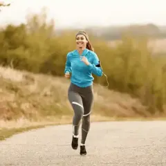 Femme souriante courant sur une route de campagne, musique dans les oreilles, pour un sport à 180 bpm.