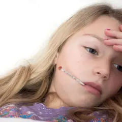 Une jeune fille malade avec un thermomètre dans la bouche, se demandant combien de temps dure la mononucléose.