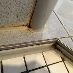 Schimmel in Fliesenfugen, oft durch Feuchtigkeit verursacht, zeigt sich als dunkle Verfärbungen. Hier sichtbar an einer Ecke mit Metallleiste.