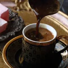Kawa po turecku, która ma najwięcej kofeiny, nalewana do ozdobnej filiżanki. Obok słodkie lokum.