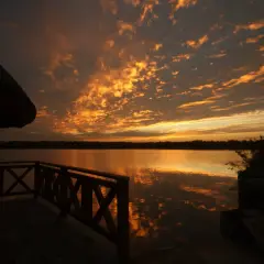 Zachód słońca nad jeziorem z widokiem na pomost i zadaszenie.