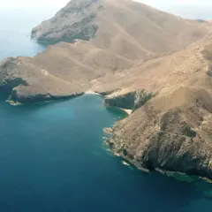 Vista aérea de la cala del bergantín, una bahía de aguas turquesas rodeada de montañas áridas y escarpadas.