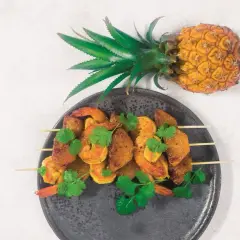 Szpadki z krewetkami i kawałkami ananasa, ozdobione kolendrą. Obok leży cały ananas, symbolizujący owoce egzotyczne.