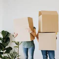 Couple déménageant, cachant leurs visages derrière des cartons. Ils préparent leur lettre changement d'adresse CAF.