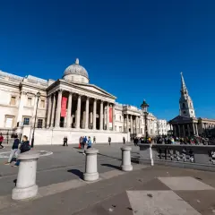 Trafalgar Square w Londynie, z National Gallery w tle. Wiele osób spaceruje po placu, ciesząc się darmowymi muzeami Londyn.