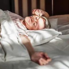 Frau erwacht lächelnd im Bett, genießt die Sonne. Erfüllt die mindest schlafzeit für Wohlbefinden.