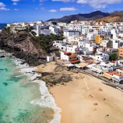 Widok na białe miasteczko na klifie i piaszczystą plażę z turkusową wodą. To urokliwa wyspa Fuerteventura.