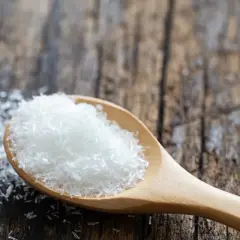 Drewniana łyżka pełna białego proszku, który może być glutaminianem sodu (MSG).