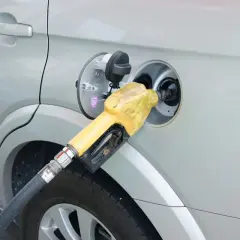 Żółta dysza dystrybutora paliwa wlewana jest do baku srebrnego samochodu. Prosty sposób, jak zatankować auto.