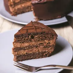 Pyszne ciasto czekoladowe ze śmietaną, z widocznym przekrojem i widelcem gotowym do degustacji.