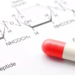 Kapsułka w kolorze czerwono-białym na tle schematu chemicznego.
