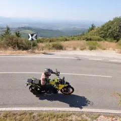 Motociclista in viaggio da Firenze a Siena, attraversa una strada panoramica tra le colline toscane sotto un cielo azzurro.