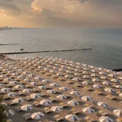Filetto di ombrelloni e lettini sulla sabbia dorata, con il mare calmo e il cielo crepuscolare a fare da sfondo. Un'immagine che evoca la tranquillità dei **Marche mare**.