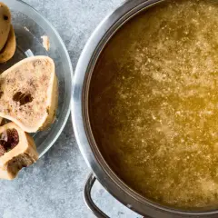 Un plato con huesos de tuétano y una olla con caldo dorado, perfecto para preparar caldo de huesos para perros.