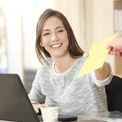 Uśmiechnięta kobieta odbiera żółtą kopertę od kuriera. Na biurku laptop i kubek.
