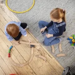 Dzieci budują tory kolejowe, angażując się w odgrywanie ról. Obok leżą klocki i inne zabawki.