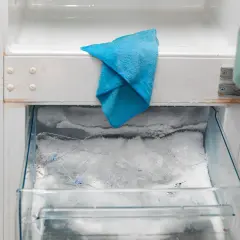 W zamrażarce lodówki no frost nagromadził się lód, a niebieska ściereczka czeka na rozmrożenie.