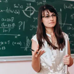 Nauczycielka matematyki w okularach, wyjaśniająca wzory na tablicy. Dofinansowanie do okularów dla nauczycieli to ważna sprawa.