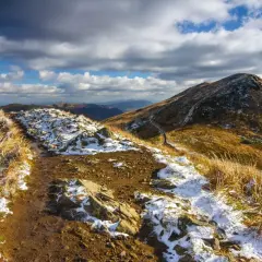 Szlak przez Bieszczady na Ukrainę, pokryty pierwszym śniegiem i jesienną trawą, pod burzowym niebem.
