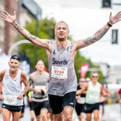 Triumfujący biegacz z tatuażami, z rękami w górze, na maratonie poniżej 2h.