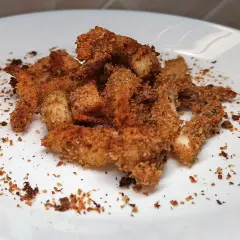 Un mucchietto di seppie gratinate al forno, dorate e croccanti, su un piatto bianco.