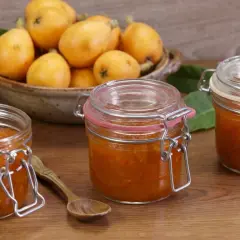 Tre barattoli di marmellata di nespole fatti in casa, con nespole fresche in una ciotola sullo sfondo.
