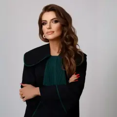 Kobieta w todze prawniczej, z rękami skrzyżowanymi na piersi, na jasnym tle.