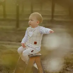 Chłopiec w beżowym, kratkowanym garniturku i muszce, siedzący na drabinie. Idealny przykład, jak ubrać dziecko na sesję zdjęciową, by wyglądało elegancko i uroczo.