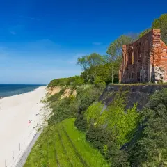 Ruiny ceglanego kościoła na klifie nad piaszczystą plażą i morzem. Idealne miejsce na weekend nad morzem.
